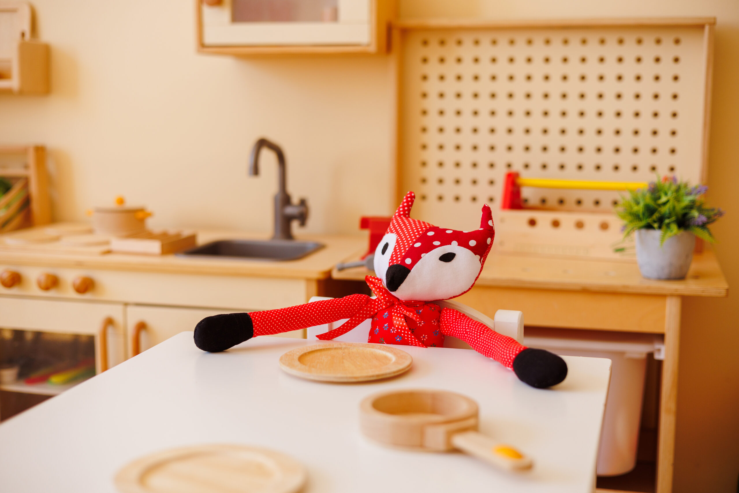 Handmade soft toy “Mr. Fox” seated at a children’s table with plates, illustrating imaginative role play in a kindergarten kitchen role-play corner