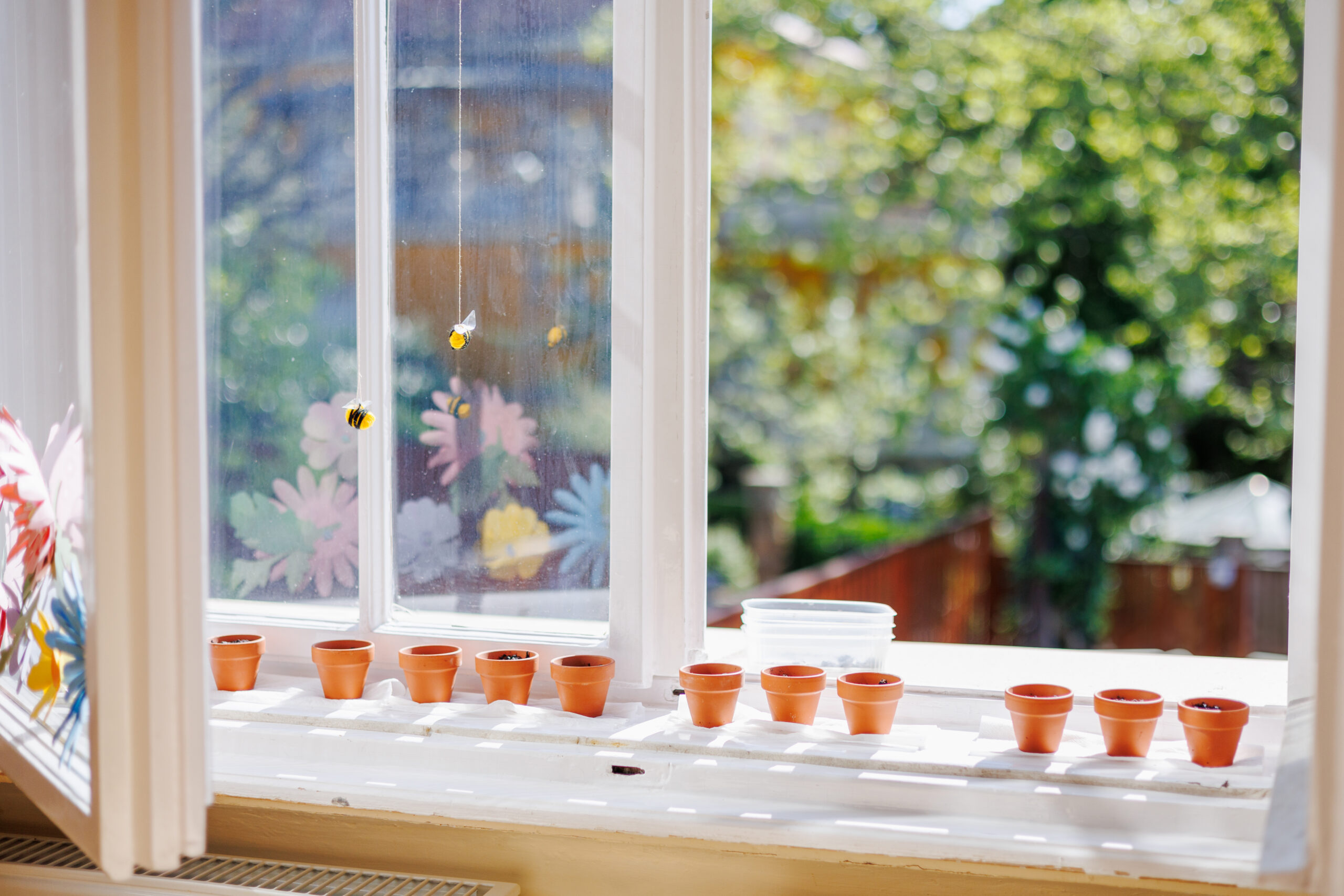 Kindergarten classroom windowsill with tiny flower pots and hanging handmade wool bees, illustrating intentional activity planning for children